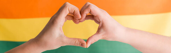 panoramic shot of woman showing heart with hands on orange, yellow and green, human rights concept 