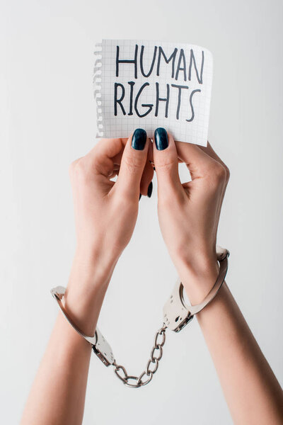 cropped view of handcuffed woman holding paper with human rights lettering isolated on white 