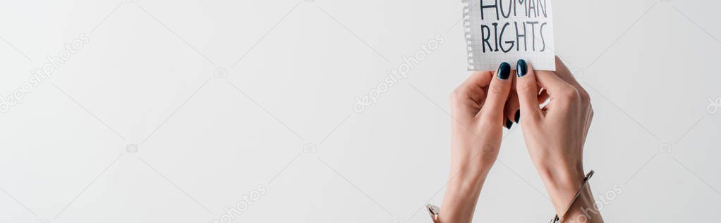 panoramic shot of woman with handcuffs on hands holding paper with human rights lettering isolated on white 