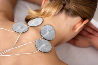 Back view of woman with electro stimulation electrodes on neck on massage couch isolated on grey clipart