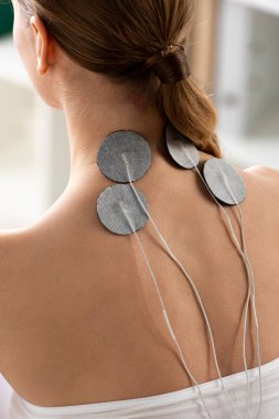 Back view of electrodes of neck of young woman during electrode treatment in clinic clipart