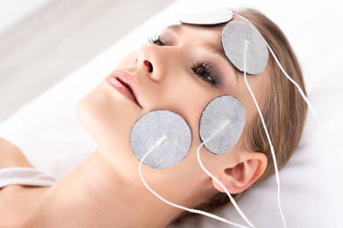 Çekici bir kadın klinikte yüz elektroterapisi sırasında masaj koltuğunda yatıyor.
