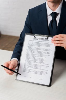 cropped view of agent holding clipboard with lease agreement lettering and pen