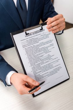 cropped view of agent holding clipboard with lease agreement lettering near desk clipart