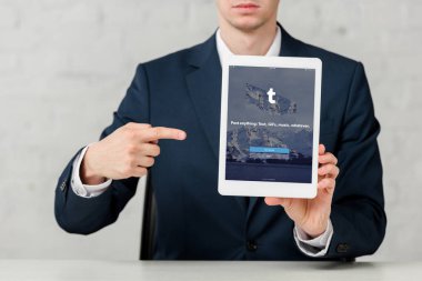 cropped view of realtor in suit pointing with finger at digital tablet with tumblr app on white 