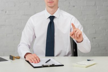 cropped view of realtor in suit pointing with finger while sitting at desk on white, leasing concept 