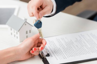 cropped view of realtor giving key to woman near carton house model, leasing concept