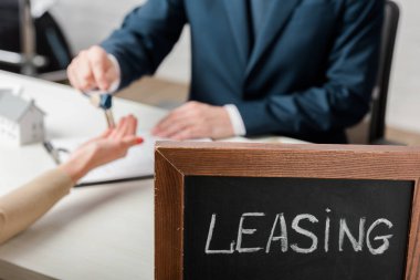 selective focus of leasing lettering on chalkboard near realtor and client 
