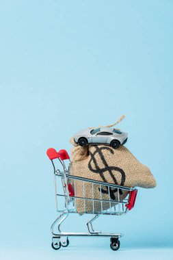 small shopping trolley with dollar bag and toy car on blue, leasing concept