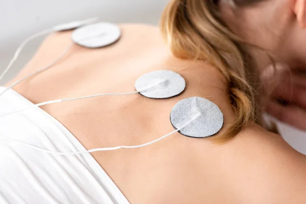 Cropped view of woman with electro stimulation electrodes on back on grey background
