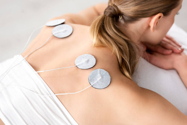 High angle view of young woman with electrodes on back during electrode treatment on grey background