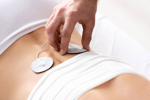 Cropped view of therapist setting electrode on patient back during electrode treatment on grey background