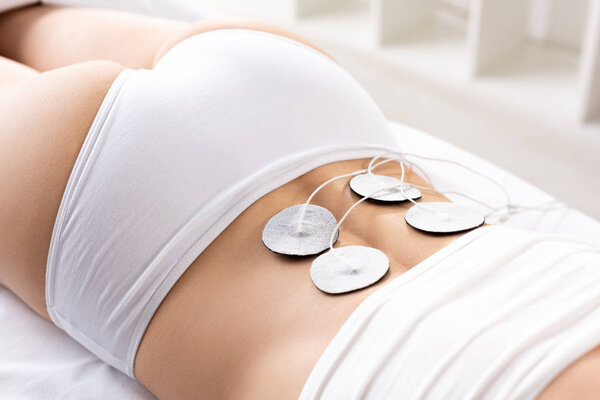 Cropped view of woman lying on massage couch during electrode treatment of lower back in clinic