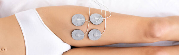 Top view of woman in panties lying on massage couch during electrode treatment of leg, panoramic shot