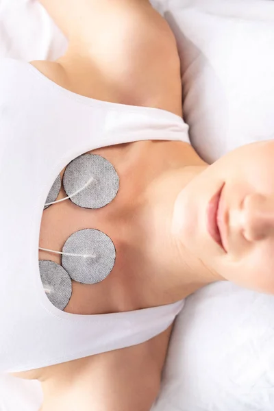 マッサージソファでの電気療法中に胸に電極を持つ若い女性のトップビュー — ストック写真