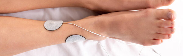 Top view of woman lying on massage couch during electrotherapy of leg, panoramic shot