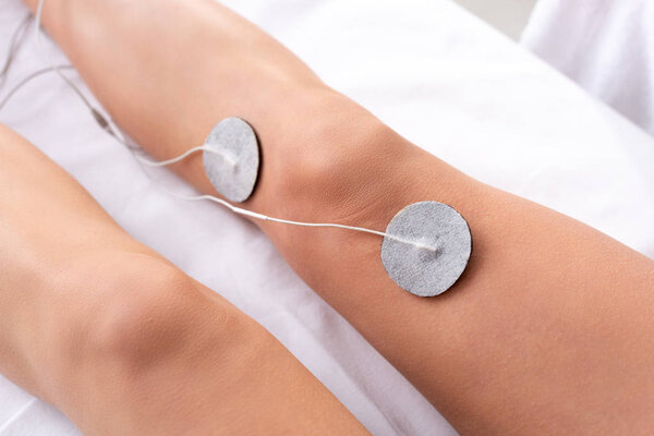 Cropped view of woman lying on massage couch during electrotherapy of knee isolated on grey