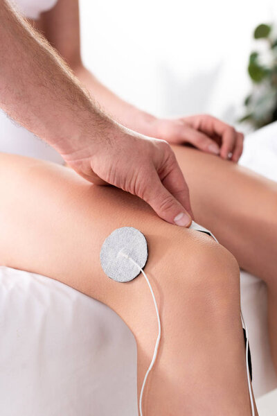 Cropped view of therapist setting electrode on knee of patient during electrotherapy