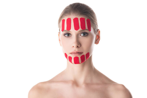 Attractive young woman with kinesiology tapes on forehead and chin looking at camera isolated on white