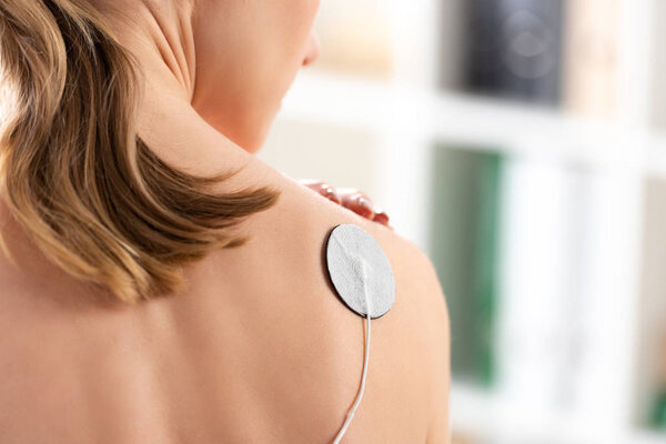 Back view of woman with electrode on shoulder during electrotherapy in clinic
