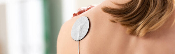 Back view of woman with electrode on shoulder during electrotherapy, panoramic shot