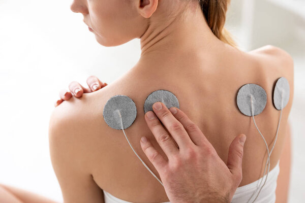 Cropped view of doctor fastening electrode on back of patient during electrotherapy in clinic