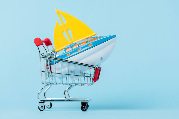 small shopping trolley with toy boat on blue, leasing concept 