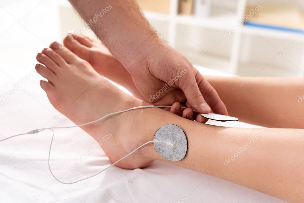 Cropped view of doctor holding electrode near patient leg during electrode treatment in clinic