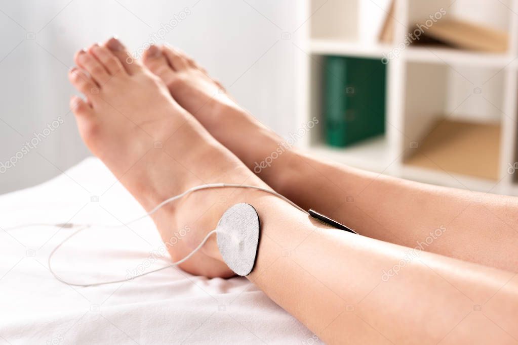 Cropped view of woman lying on massage couch with electrodes on leg in clinic