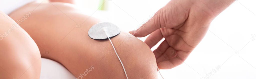 Cropped view of therapist setting electrode on knee of patient on white background, panoramic shot