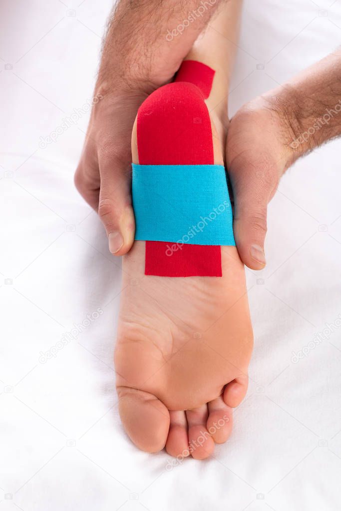 Cropped view of dactor applying kinesiology tapes on heel of patient on massage couch