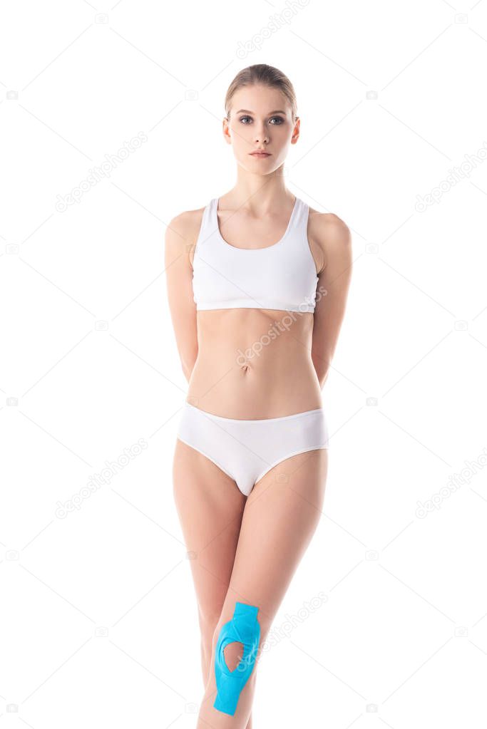 Beautiful girl in underwear with kinesiology tapes on knee looking at camera isolated on white