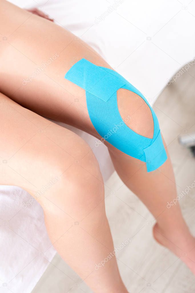 Cropped view of woman with kinesiology tapes on knee sitting on massage couch in clinic