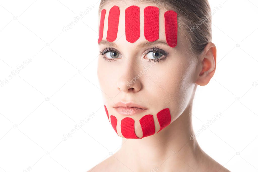 Beautiful girl with kinesiology tapes on chin and forehead looking at camera isolated on white