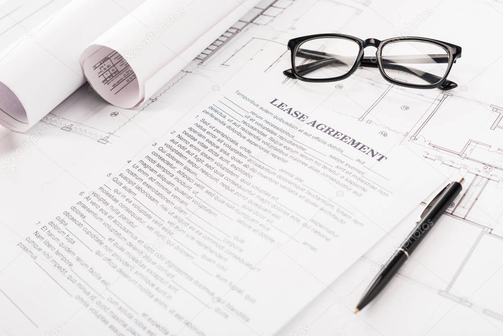 document with lease agreement lettering near glasses, blueprints and pen on desk 