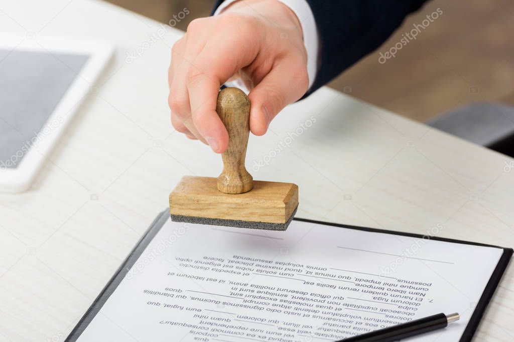 cropped view of realtor holding stamp near clipboard with document on table, leasing concept 