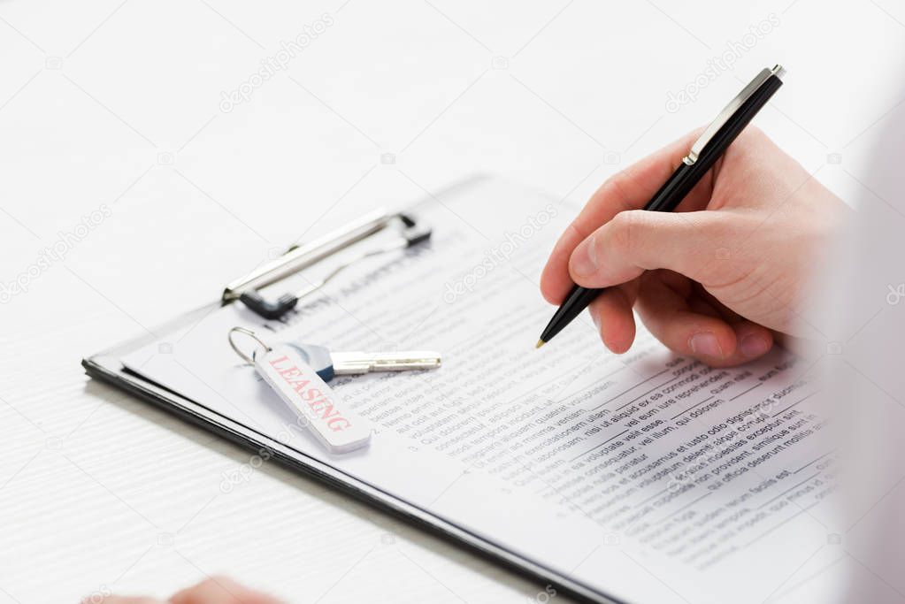 cropped view of realtor holding pen near clipboard with document and key with leasing lettering 