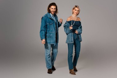 Gri arka planda kot ceketli ve kot pantolonlu gülümseyen adam ve kadın 