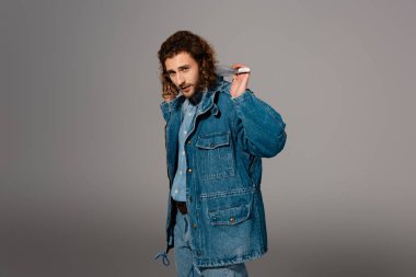 Kot ceketli ve kot pantolonlu yakışıklı ve şık bir adam gri üzerinde şemsiye tutuyor.