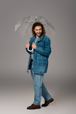 Kot ceketli gülümseyen adam ve gri arka planda şemsiye tutan kot pantolonlu adam. 