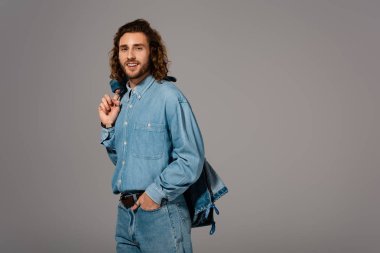 Kot gömlekli ve kot pantolonlu gülümseyen adam gri üzerine izole edilmiş bir ceket tutuyor.