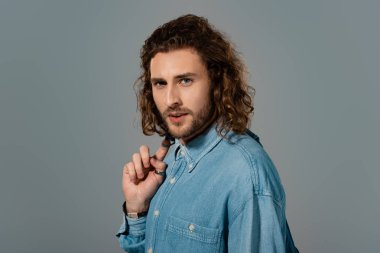 Kotlu gömlekli yakışıklı ve şık bir adam gri renkli kameraya bakıyor.