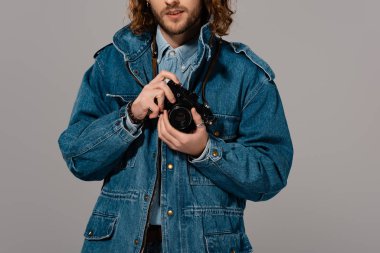 Gri renkte dijital kamera tutan kot ceketli adam görüntüsü.