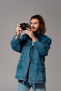 Kot ceketli ve kot pantolonlu yakışıklı ve şık bir adam gri üzerinde fotoğraf çekiyor.