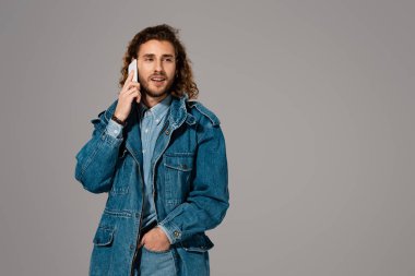 Kot ceketli yakışıklı ve şık bir adam gri renkte izole akıllı telefondan konuşuyor.
