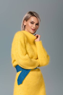Sarı elbiseli çekici ve gülümseyen bir kadın gri renkli kameraya bakıyor.