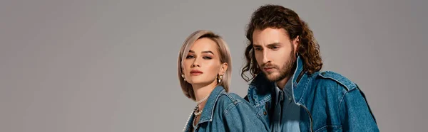 panoramic shot of stylish man and woman in denim jackets isolated on grey