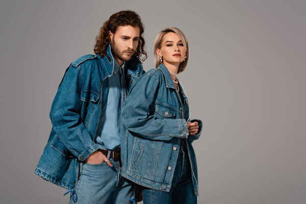 stylish man and woman in denim jackets looking at camera isolated on grey