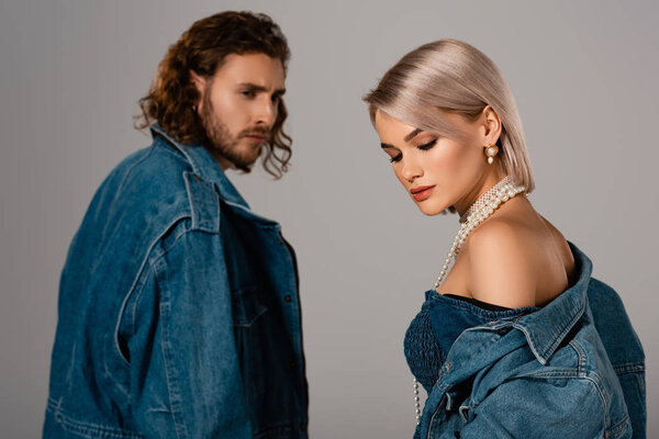 селективный фокус стильного мужчины, смотрящего на женщину в джинсовой куртке, изолированной на сером
