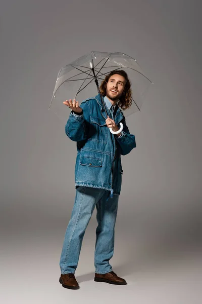 デニムジャケットの笑顔男とグレーの背景に手を伸ばして傘を持っているジーンズ — ストック写真